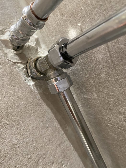 VVS-installation med synliga rör och sprickor vid genomföring utan täckbricka i betongvägg.