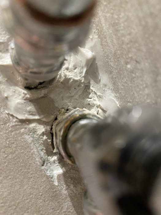 Närbild av rör i vägg med synlig kalkavlagring och sprickor runt rörgenomföring.