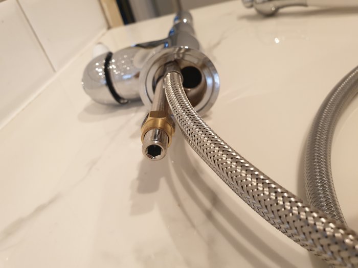 Utdragbar duschslang och koppling av märket Bugnatese på badrumsbänk med en guld-mutter.