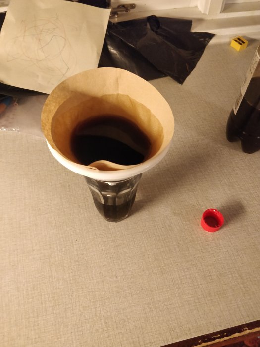 Tratt med kaffefilter silandes årgångs-Dunderglögg i ett glas på ett köksbord.