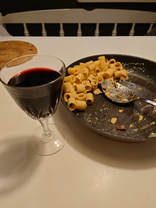 Efterrätt på pasta carbonara med bacon och äggula i stekpanna bredvid ett glas rött vin.