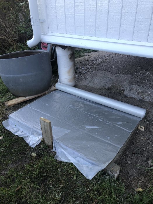 Nyutgjuten betongplatta täckt med plast vid husgrund för installation av värmepump.