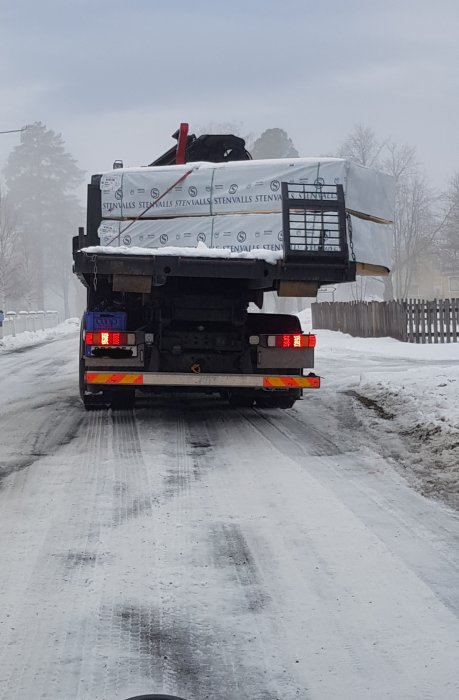 Lastbil med snötäckt flak och spännband på en vinterväg.