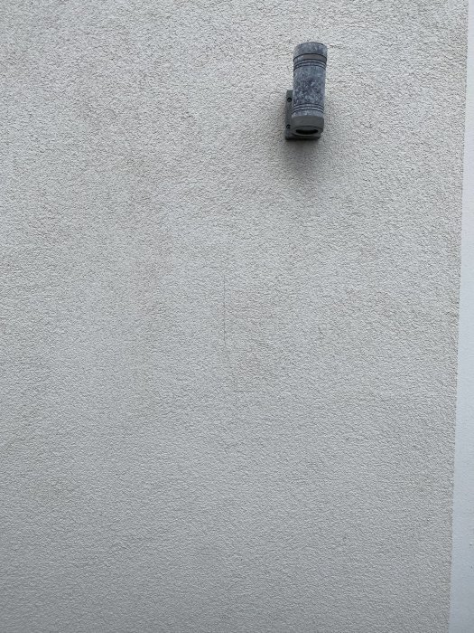 En närbild på en vit fasad med en vertikal spricka under en utomhuslampa, på ett stenhus byggt 2007.