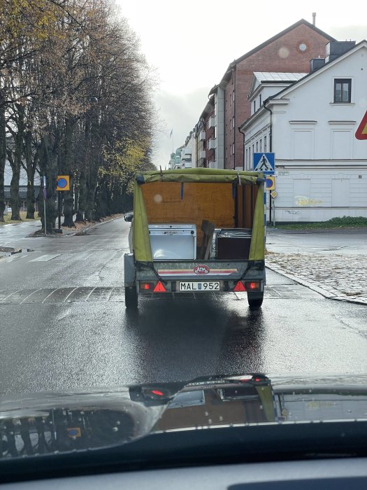 Lastbilssläp med osäkrade föremål på en blöt gata, sett från ett bilfönster.