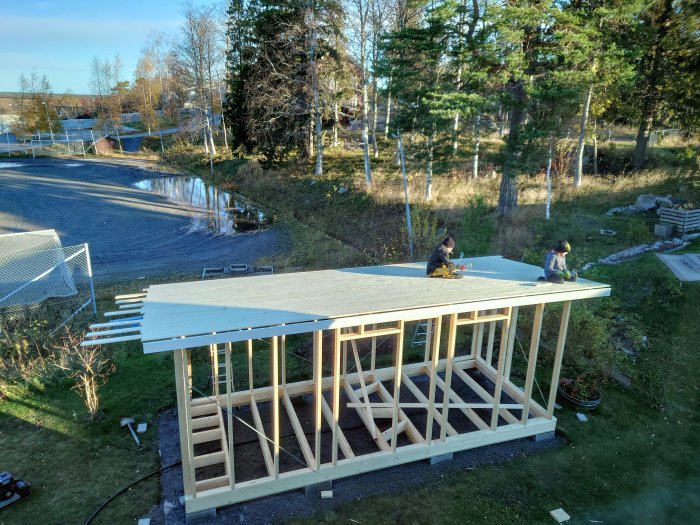 Två barn hjälper till att spika råspont på taket till en friggebod under konstruktion.