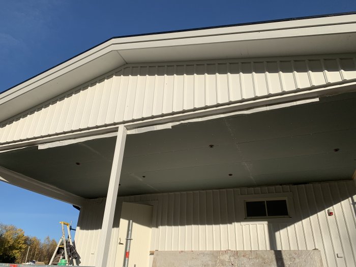 Carport med klätt tak med utegips, elektriska förberedelser synliga och stege till vänster.