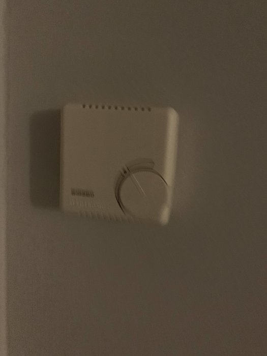 Wirsbo väggtermostat inställd på en hög temperatur i ett mörkt rum.