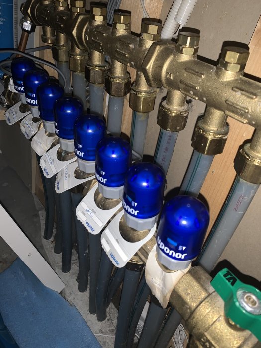 Golvvärmefördelare med blå reglerventiler, etiketter och kopplade rör.