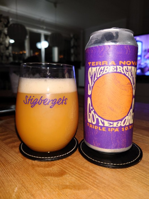 En Stigbergets ölburk bredvid ett glas öl, på ett bord med inredning i bakgrunden.