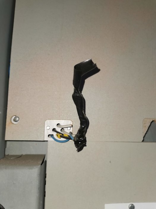 Elkabel med isoleringstejp hängande från öppet eluttag på en vägg.