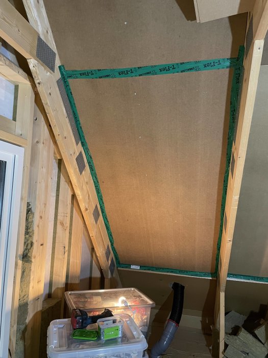 Luftspalt konstruerad med board fasttejpad vid takstolarna, redo för isolering med lösull, verktyg och material synligt.