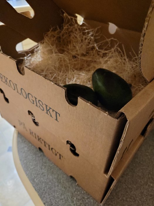 En mogen avokado i en öppen låda märkt "Ekologiskt" med skyddande stråmaterial.