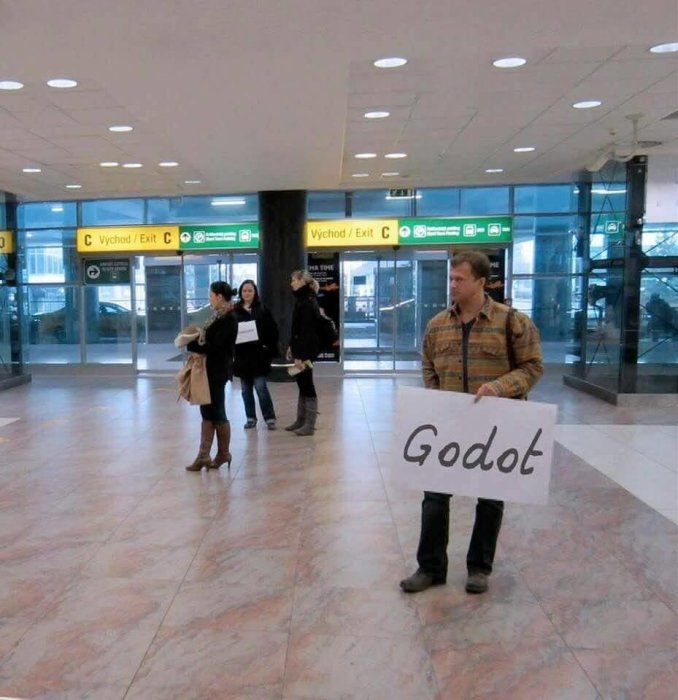 Person som håller skylt med texten "Godot" i en terminalbyggnad.