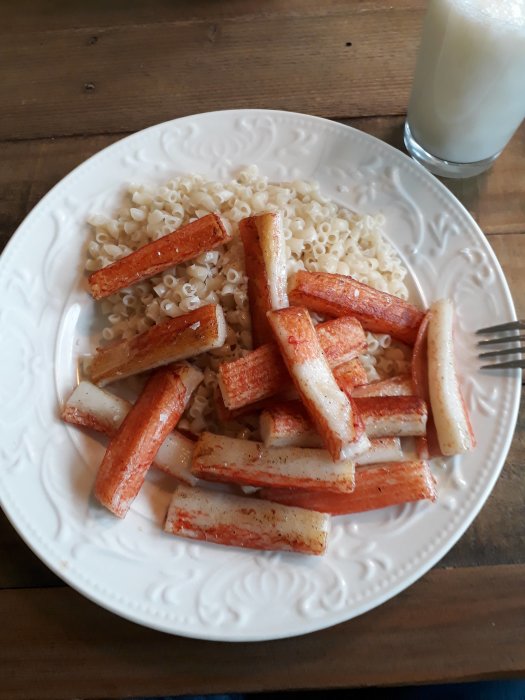 Tallrik med snabbmakaroner och stekta crabsticks, bredvid ett glas mjölk.
