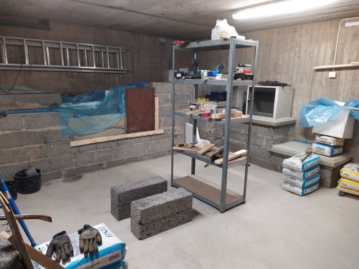 Ett renoveringsskede i källare med betongblock, hyllor och byggmaterial.
