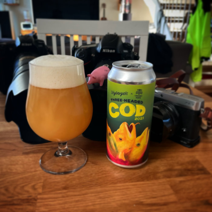 Ett glas öl med skum och en ölburk med texten "COD 2021", omgivet av kamerautrustning.