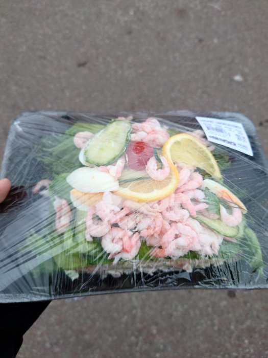 Hand håller en förpackad skaldjurssallad med räkor, citron och gurka.