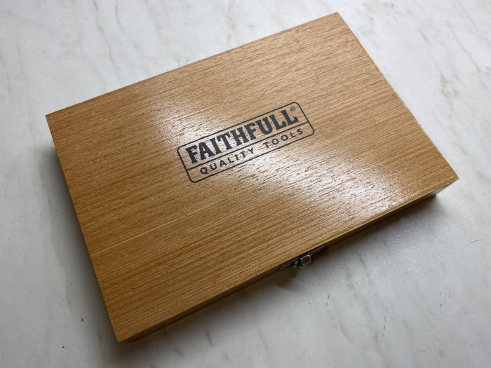 Trälåda med texten "FAITHFULL QUALITY TOOLS" tryckt på locket, antydan om verktygsset inuti.