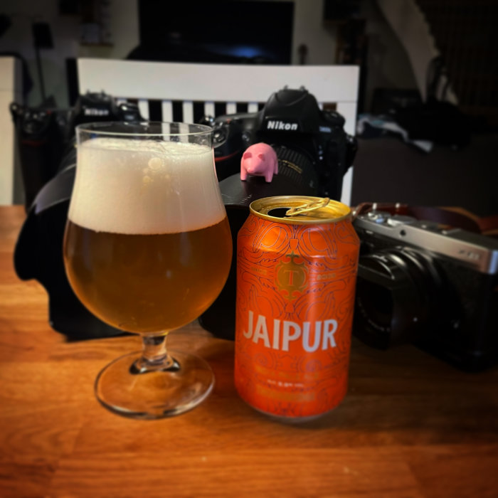 Ett glas öl bredvid en öppnad burk JAIPUR och två kameror i bakgrunden.