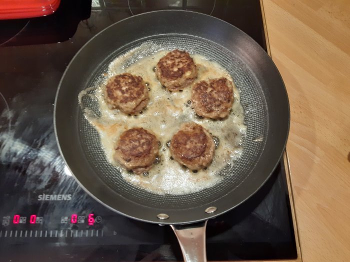 Sex stekta vildsvin och älgfärsbiffar i stekpanna på spis.