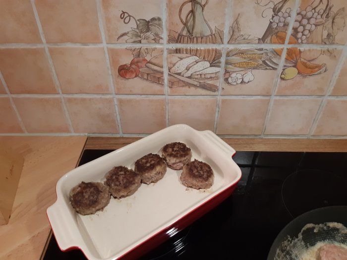 Fem nyformade vildsvin och älgfärsbiffar på en röd ugnsform, redo att stekas.