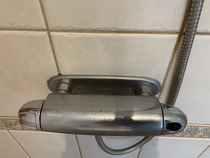 Duschblandare monterad på kakelvägg med synlig röranslutning och vattenavlagringar.