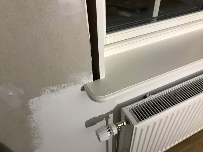 En omonterad tapet bredvid ett fönster och en vit radiator, med synlig vägg där tapeten ska skäras till.