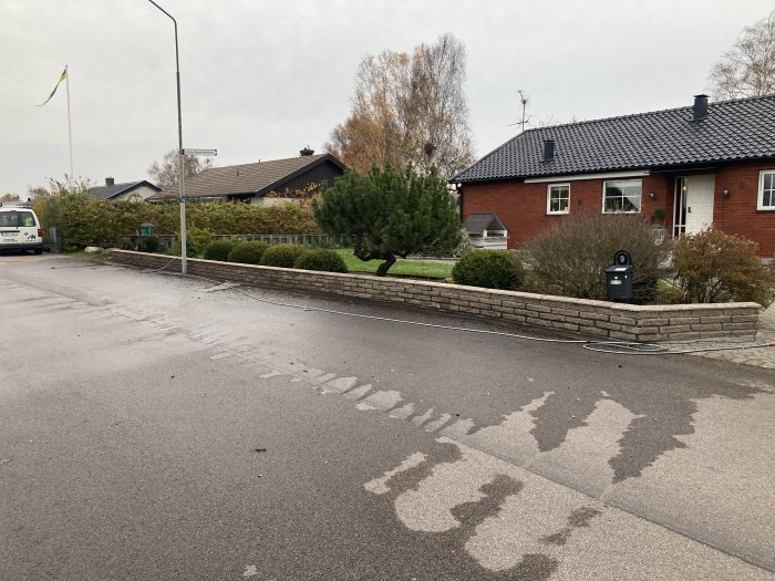 Nyligen tvättad stenmur framför ett rött tegelhus vid en gata med blött trottoar från rengöringen.