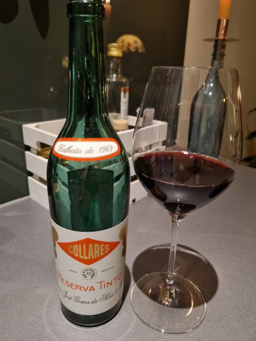 Flaska gamla Colares Reserva Tinto 1969 bredvid ett glas med rött vin på ett bord.