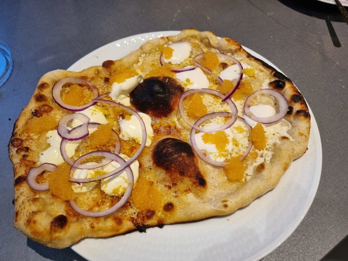 Hembakad pizza med ojämn gräddning och halva med mjölkfri ost, toppad med rödlök och orange färgade tillbehör.