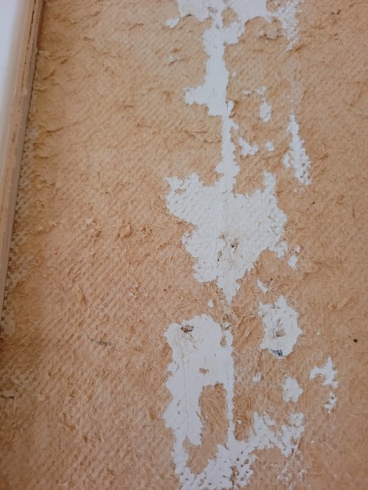 Närbild på tretex-vägg med luddiga rester av gammal vit färg som flagar av.