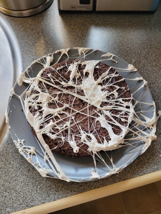 Chokladkaka drizzlad med vit glasyr på en grå tallrik, kantad av bakplåtspapper.