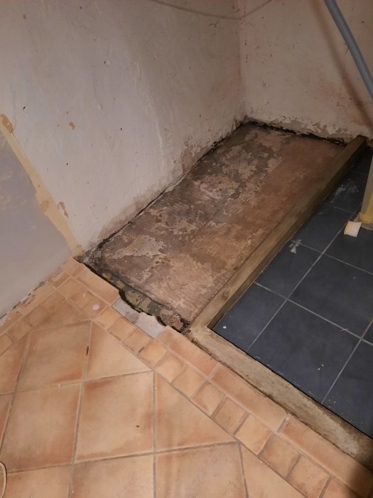 Hörn av ett rum med en nygjuten betongplatta nära väggen och isolerade kablar som löper på väggen.