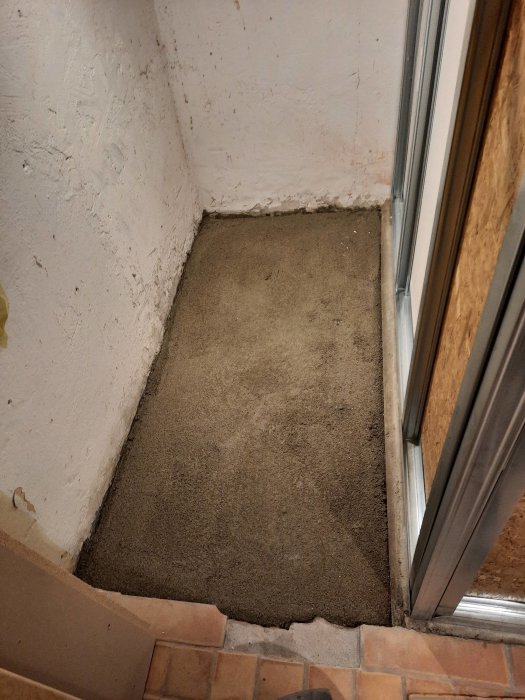 Nyformad betongplatta i hörn av rum, omgiven av vita väggar och tegeltrappsteg.