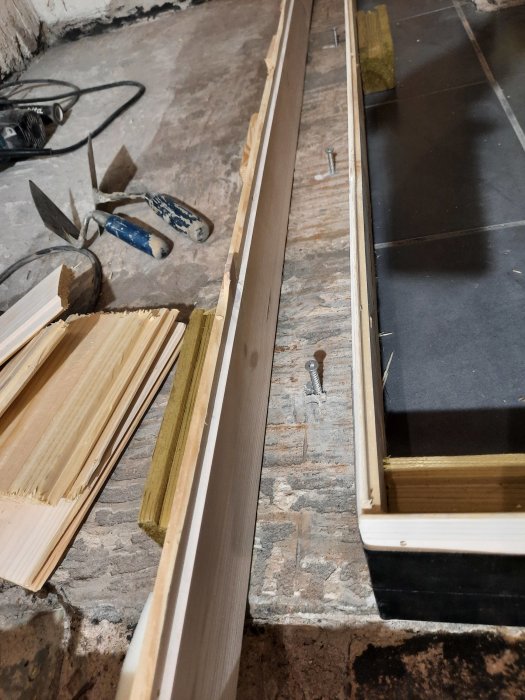 Enkel träform för gjutning med panelbrädor, klossar och smältlim på ett betonggolv.