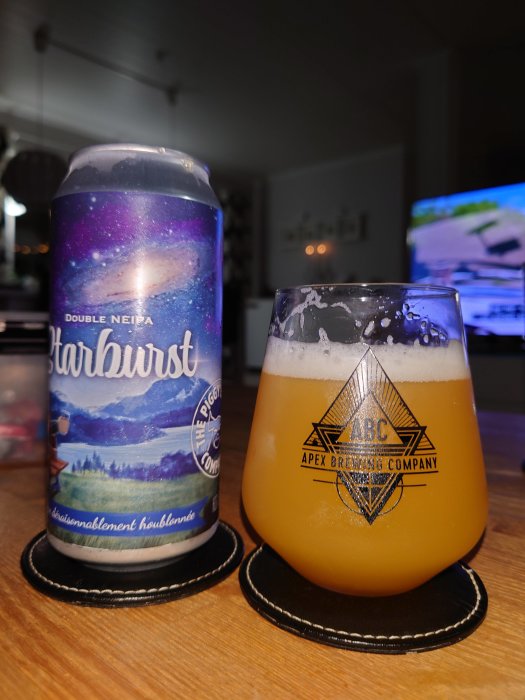 Ölburk med rymd- och landskapsdesign bredvid ett glas fyllt med öl på bordsunderlägg.