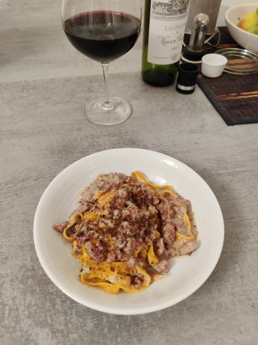 Tallrik med tryffelpasta och riven tryffel, ett glas rödvin och en vinflaska i bakgrunden.