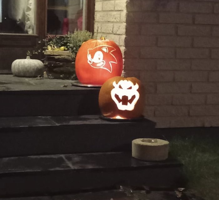 Två upplysta halloweenpumpor med uthuggna motiv på en trappa utomhus på kvällen.