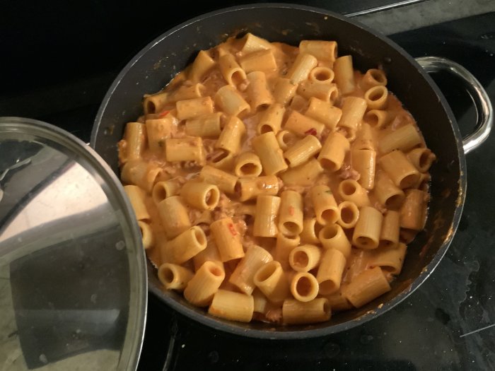 En stekpanna med nykokt salsicciapasta i sås med chili och pecorino på en spishäll.