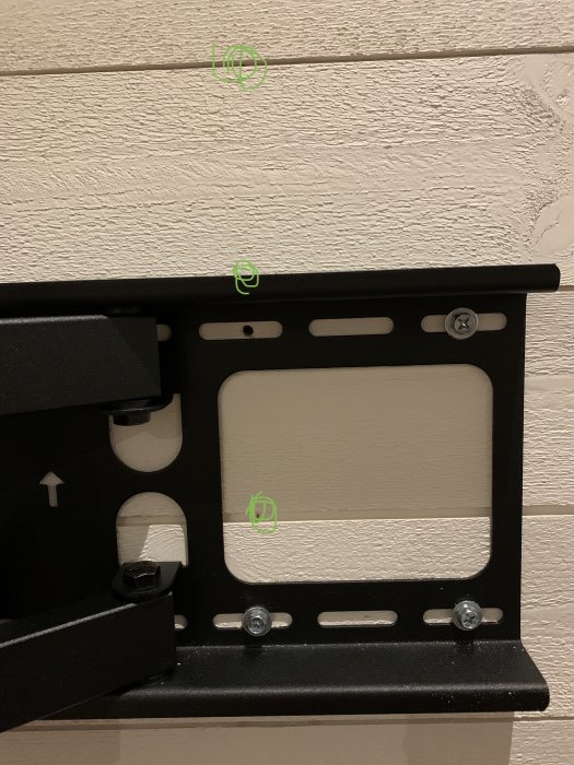 Väggfäste för TV monterat på panelvägg med synliga skruvhuvuden och markerade punkter där snickare fäst panelen.