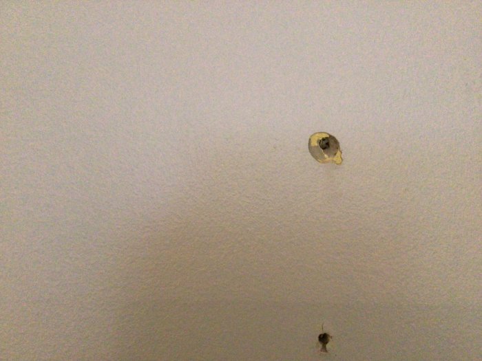 Vägg med dåligt fäst skruvhål och bygglim runt, indikerar problem med installation av hyllor.