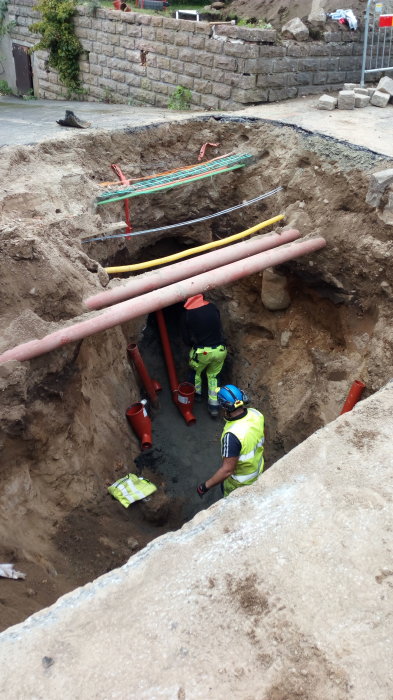 Arbetare gräver upp och reparerar rörledning för avlopp i en grävd grop.