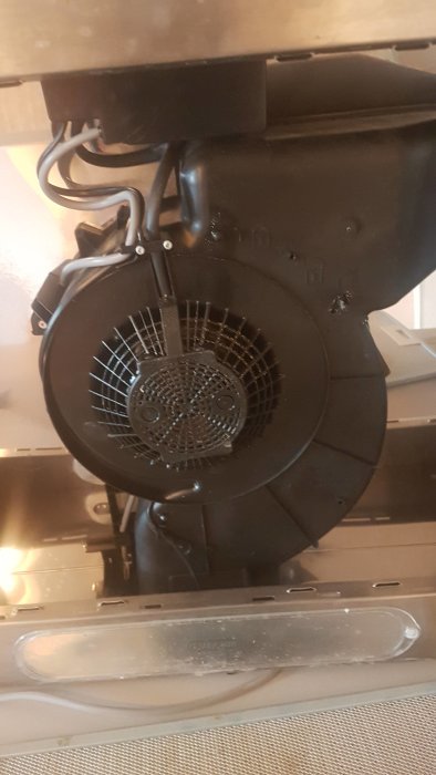 Insida av en köksfläkt med synlig motor och rund metallgaller som eventuellt är ett kolfilter.