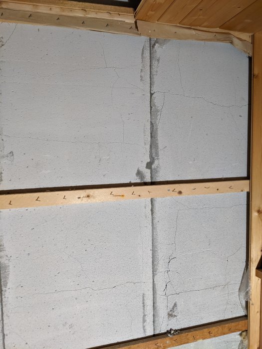 Ødelagte letbetonvægge med revner og skader i et duschrum under renovering, monteret med trærammer.