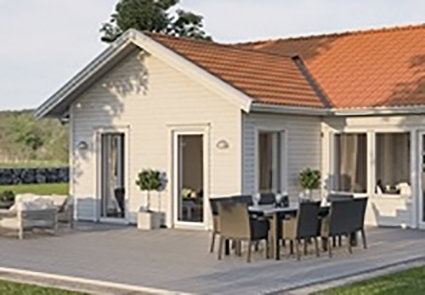 Enplansvilla med utbyggnad som visar extra fönsterpartier, terrass med möbelgrupp under tak.