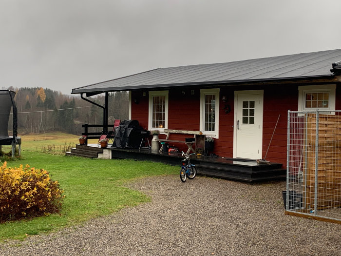 Röd enplansvilla med svart tak och veranda, potentiell utbyggnadsyta synlig.