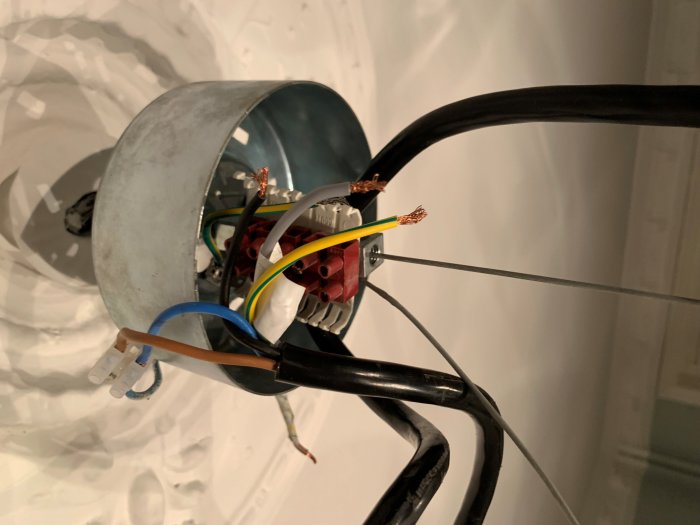 Elektriska trådar och kopplingsklämma inuti en lampa för diskussion om dragavlastning och installation.