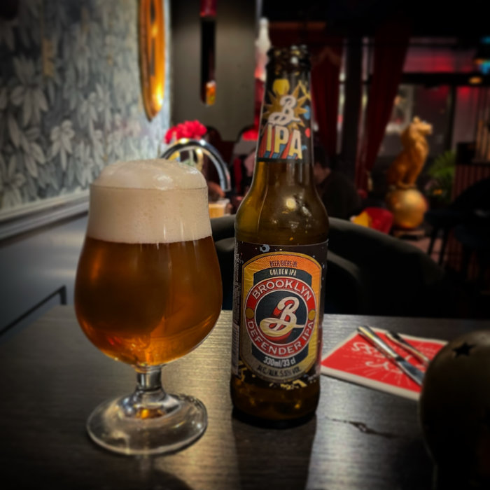 En öl i ett glas och en tom ölflaska på ett bord i en bar, med suddig bakgrund.