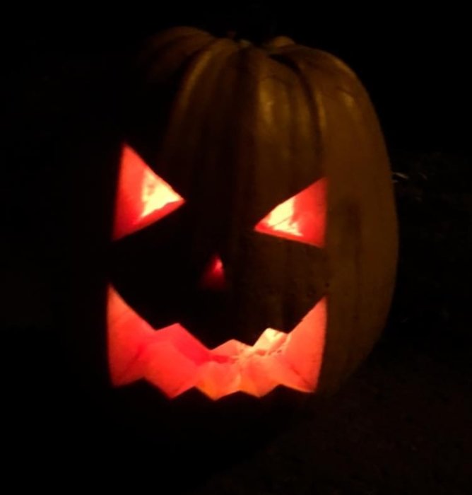 Upplyst halloweenpumpa med urkarvade ögon och mun i mörker.